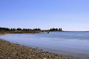 A calm river with a rocky shoreline and trees in the background.