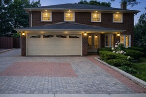 A two-story house with a garage, brick exterior, and a well-maintained front yard with hedges and flowers. - Private Room in North York | Shared Bath (Toronto)