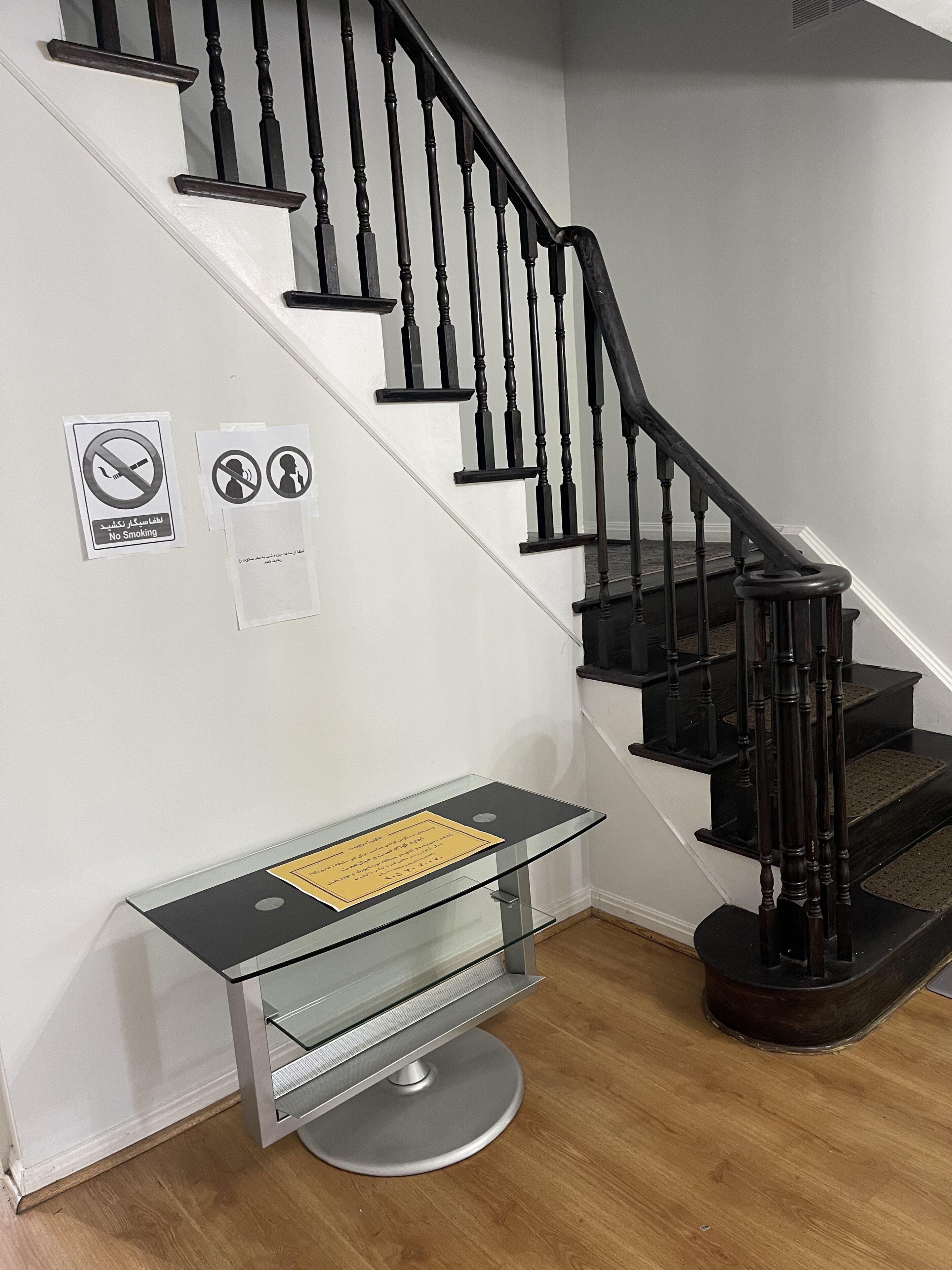 Eine Treppe mit schwarzen Spindeln, ein Glastisch mit einer gelben Schilder und zwei Rauchverbotsschildern an der Wand.