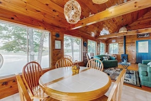 A wooden cabin interior with a dining table, chairs, a sofa, and a fireplace.
