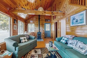 A cozy cabin interior with two sofas, a fireplace, and a large window.