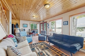 A spacious living room with a wooden ceiling, large windows, and a view of a lake.