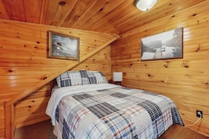 A wooden cabin bedroom with a bed, two framed pictures, and a nightstand.