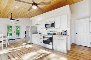 A modern kitchen with white cabinets, stainless steel appliances, and a wooden ceiling. - Modern Maine cottage with river views, deck, and a convenient washer/dryer (Stockton Springs)