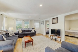 A spacious living room with a sofa set, a coffee table, a TV, and a large window.