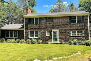 A two-story house with a brick exterior, green shutters, a green door, and a well-maintained lawn.