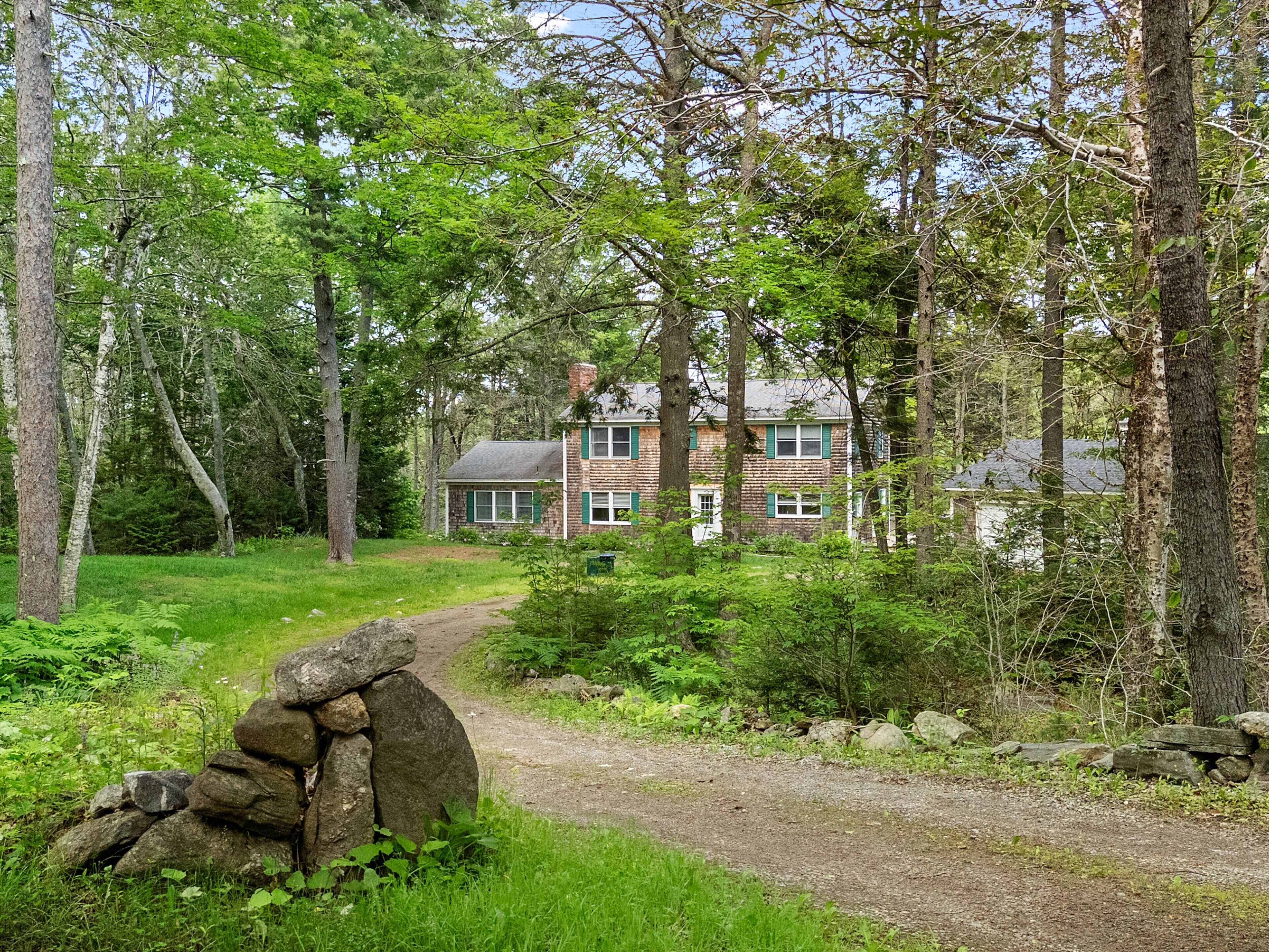 Ein rustikaler Steinweg führt zu einem Ziegelhaus, umgeben von dichtem Wald.