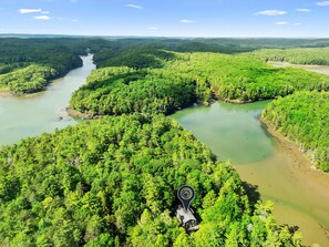 Un río serpentea por una zona boscosa con una cabaña y un puente.