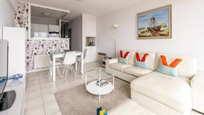 Un salón moderno con un sofá blanco, una mesa de comedor y una cocina al fondo.