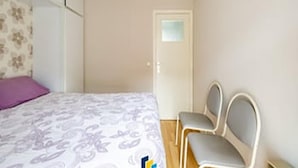 Un dormitorio con una cama, dos sillas, una puerta y una ventana.