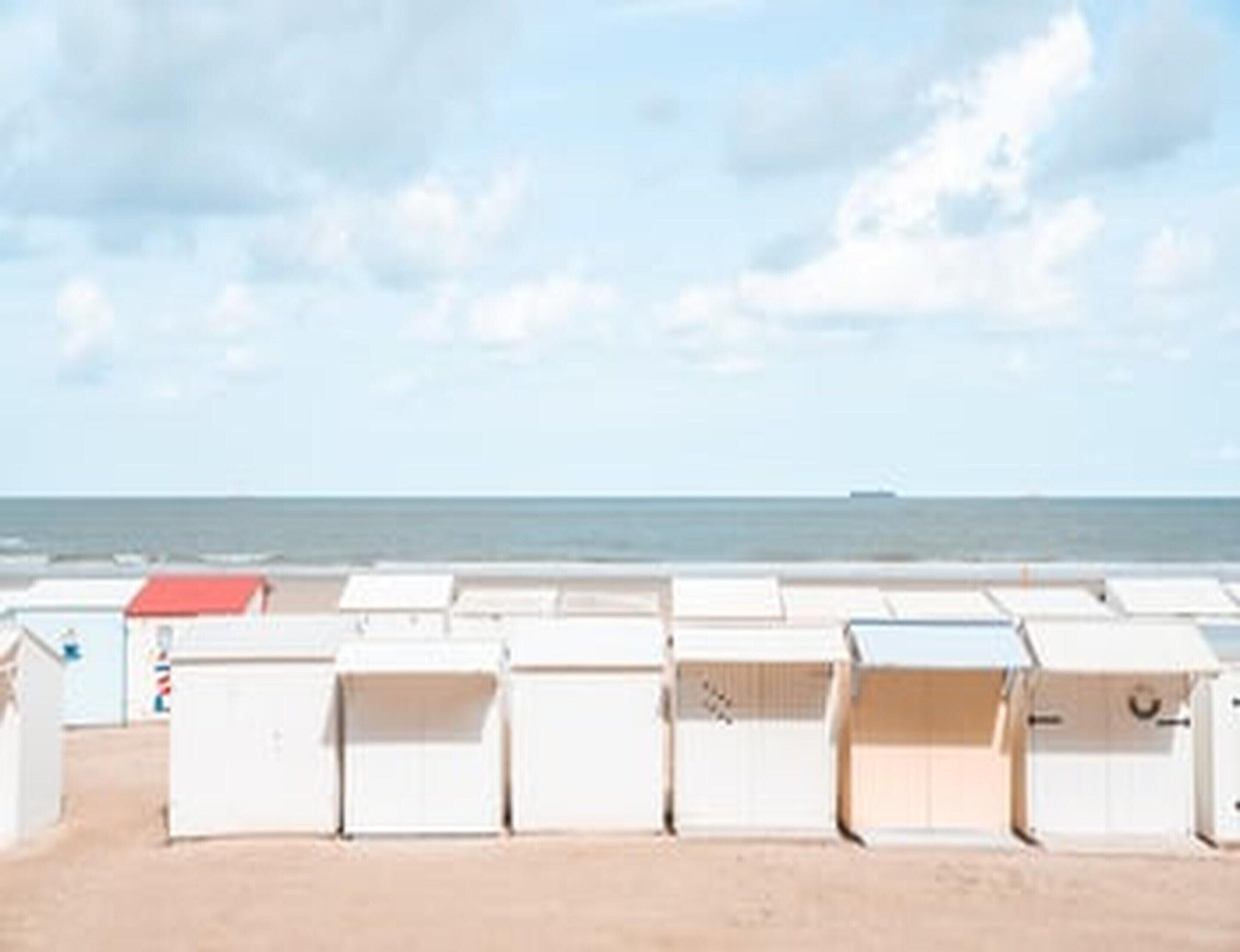 Een rij witte strandhutten met een zandstrand en de zee op de achtergrond.