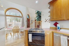 A kitchen with wooden cabinets, a stove, and a dining area with a table and chairs. - High View- Serene waterfront home w/ a dock, large deck & amazing views! (Harpswell)