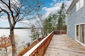 A wooden deck with a railing, overlooking a body of water and trees. - High View- Serene waterfront home w/ a dock, large deck & amazing views! (Harpswell)