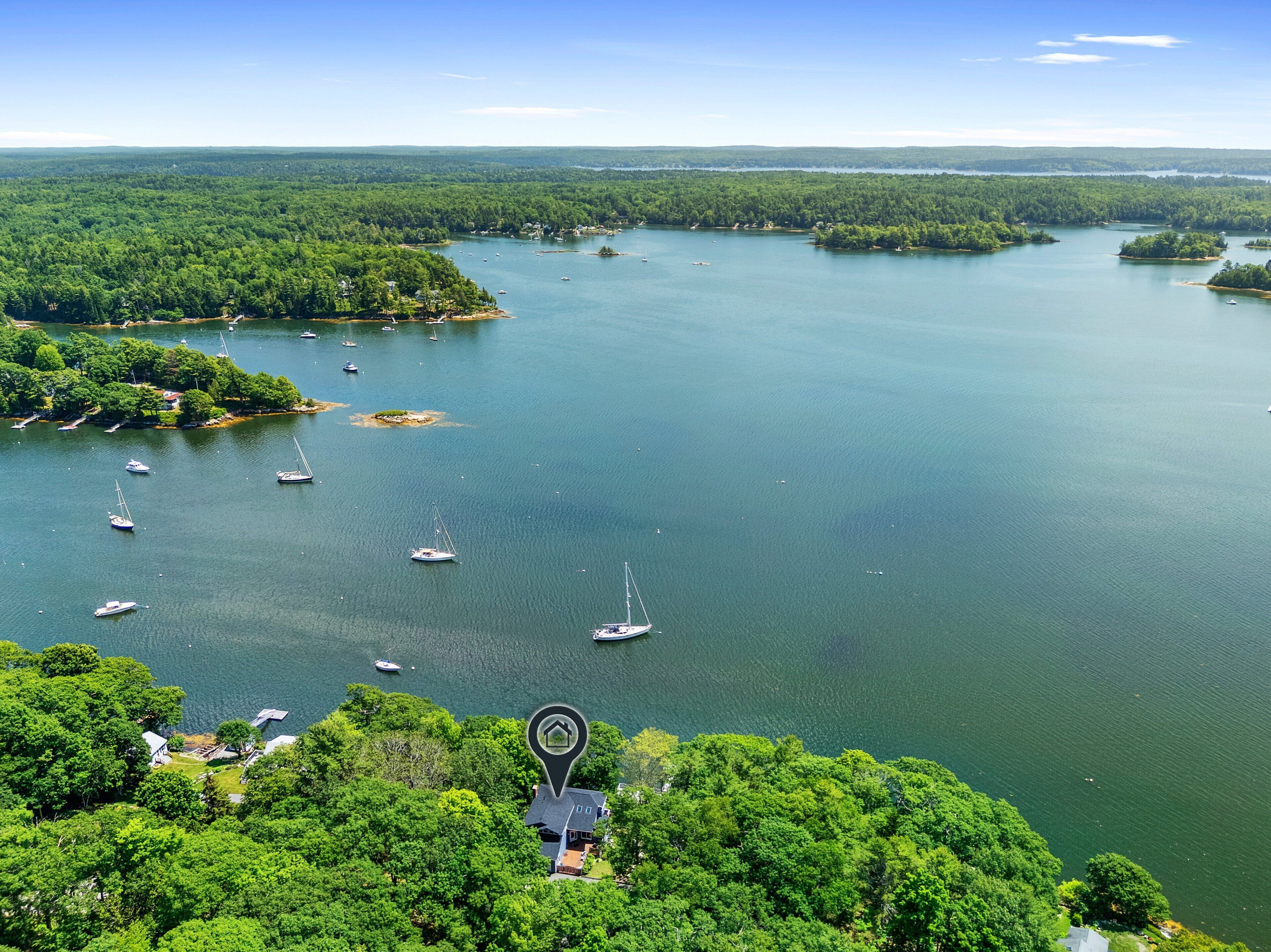 A large body of water with multiple boats, surrounded by dense green forest and a clear sky.