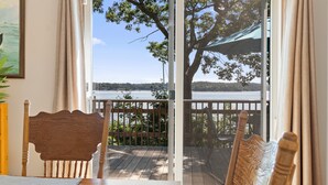 A room with a wooden table, a chair, a view of a lake through a sliding glass door, and a wooden deck outside. - High View- Serene waterfront home w/ a dock, large deck & amazing views! (Harpswell)