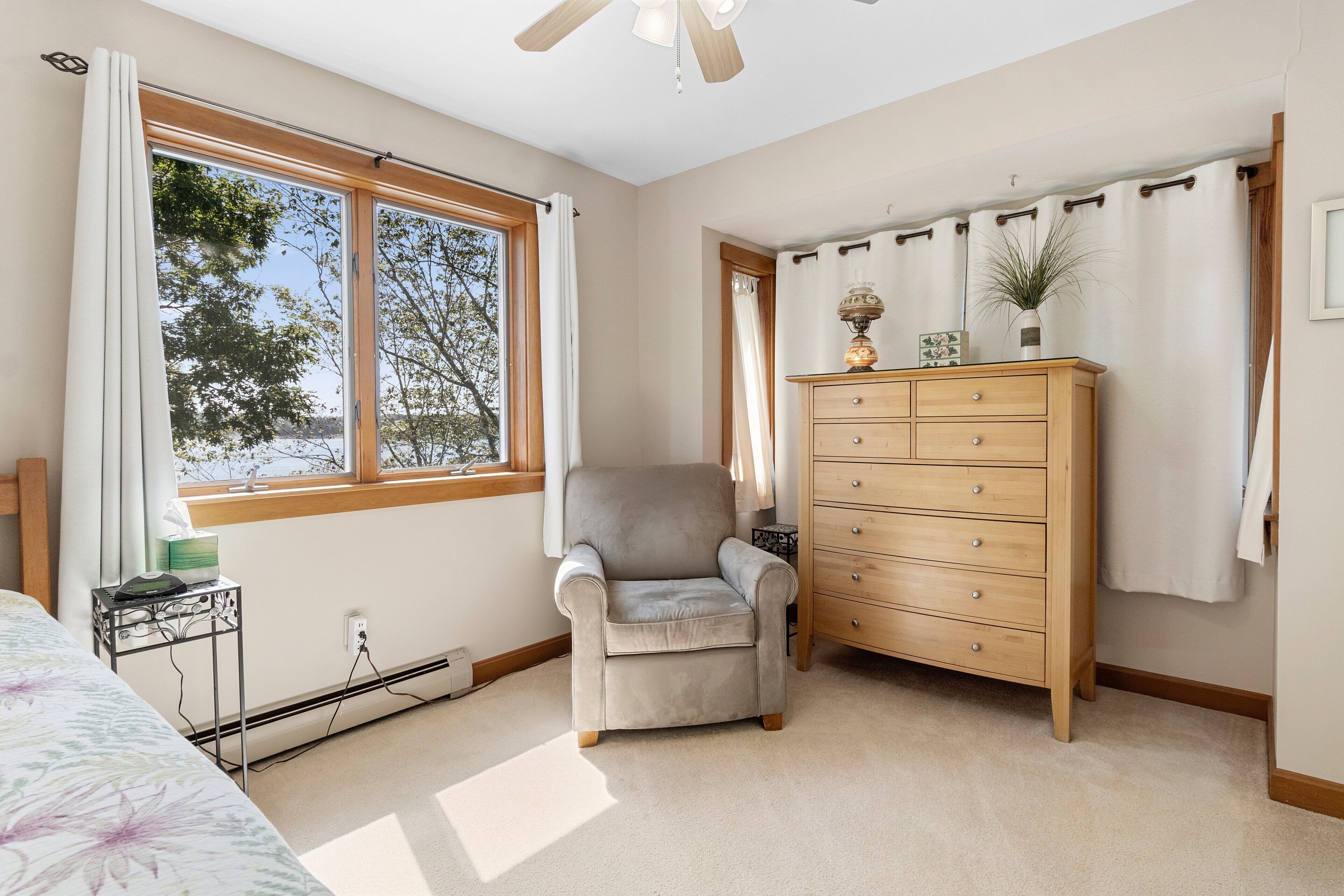 Quarto com cama, uma cadeira, cômoda e janela com cortinas.