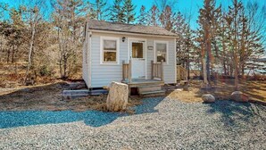 A small, single-story cabin with a front porch, surrounded by trees. - Charming love shack with stunning seaside views and all the comforts of home (Trenton)