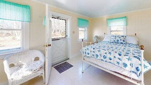 A bedroom with a bed, a chair, a door, and windows with curtains. - Charming love shack with stunning seaside views and all the comforts of home (Trenton)