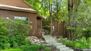 A wooden house with a porch, surrounded by lush greenery and a wooden staircase leading to the entrance. - Ledgewood 9 - Charming Cottage near Seal Harbor Beach and hiking trails (Mount Desert)