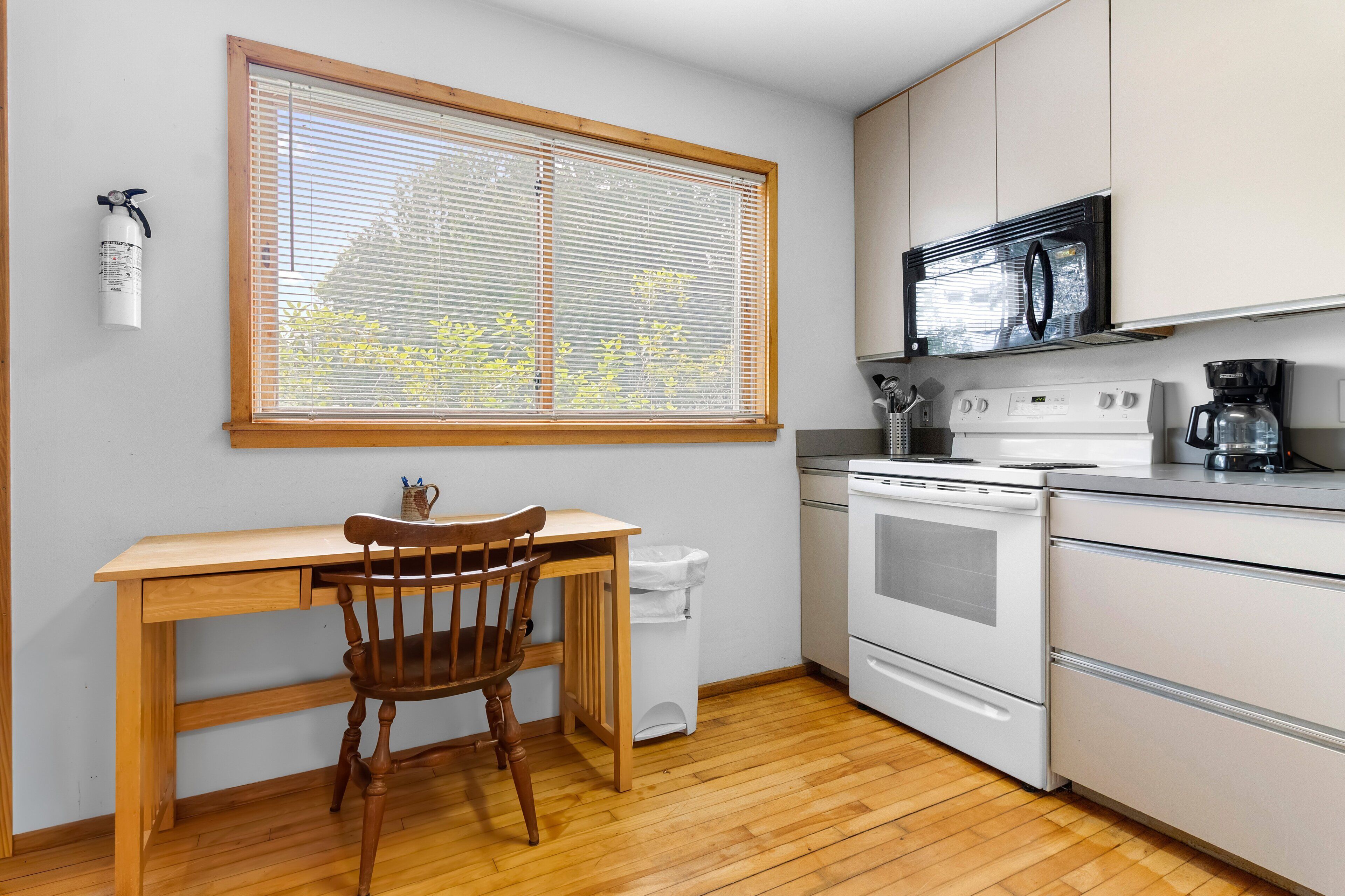 A compact kitchen with a wooden table, a chair, a microwave, an oven, and a coffee maker.