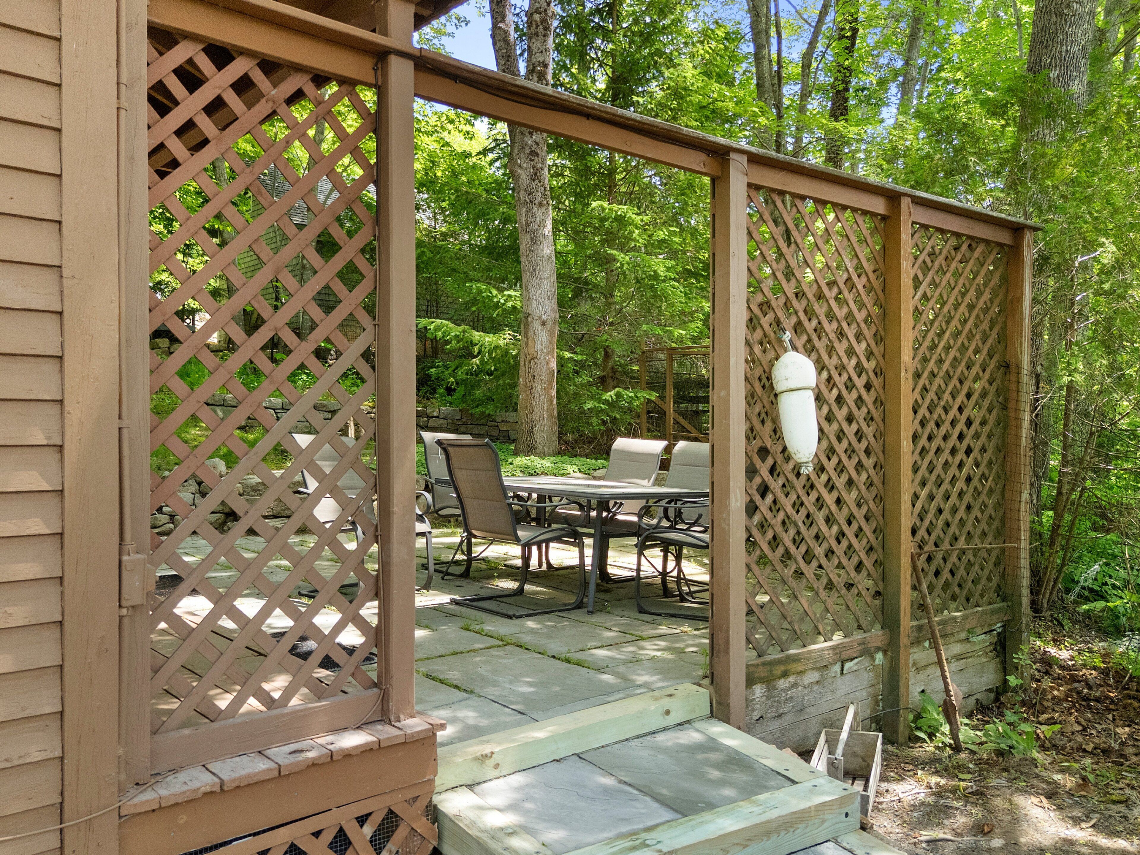 Un patio couvert, équipé d’une table et de chaises, entouré d’une clôture en treillis de bois.