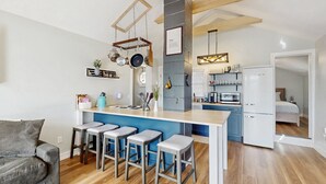 A modern kitchen with a central island, bar stools, hanging pots, and a built-in microwave.