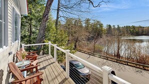 A wooden deck with chairs and a table, overlooking a lake and forest.