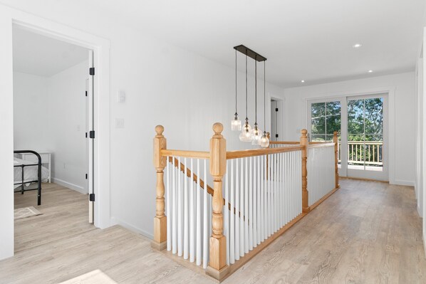 Un interior moderno con escalera de madera, barandillas blancas e iluminación colgante.