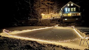 A house with a snow-covered yard, a deck, and string lights. - Idyllic Lakefront Retreat:  pvt dock & beach for kayaking, swimming & fishing (Swanville)