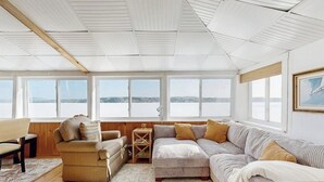 A room with a large window, a sofa, a chair, and a small table. - Idyllic Lakefront Retreat:  pvt dock & beach for kayaking, swimming & fishing (Swanville)