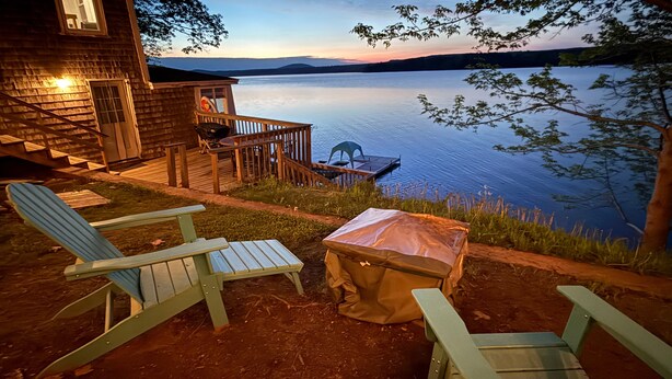 A lakeside cabin with a deck, outdoor seating, and a view of the water. - Idyllic Lakefront Retreat:  pvt dock & beach for kayaking, swimming & fishing (Swanville)