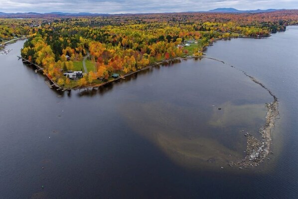 An aerial view of a lake surrounded by autumn-colored trees and a small island with a dock.