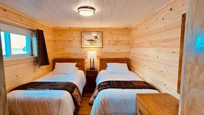 Una camera in una casetta di legno con due letti, un comodino con una lampada e un quadro appeso al muro.