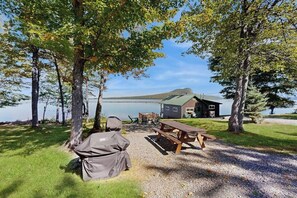 Een vakantiehuisje aan het meer met een picknicktafel en barbecue, omringd door bomen en uitzicht op het water.