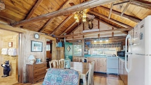Un interno rustico con un tavolo da pranzo in legno, una panca, un angolo cottura con lavello e fornello, e un soffitto con travi a vista.