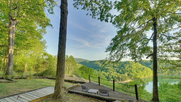 A wooden deck with chairs and a table overlooking a lake, surrounded by trees.
