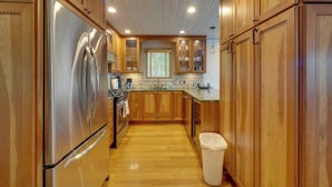 A kitchen with wooden cabinets, a stainless steel refrigerator, and a trash bin.