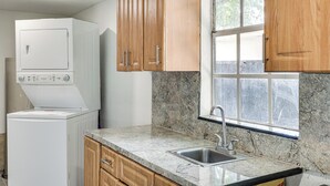 Una cocina con lavadora incorporada, encimera de granito, armarios de madera y una ventana.
