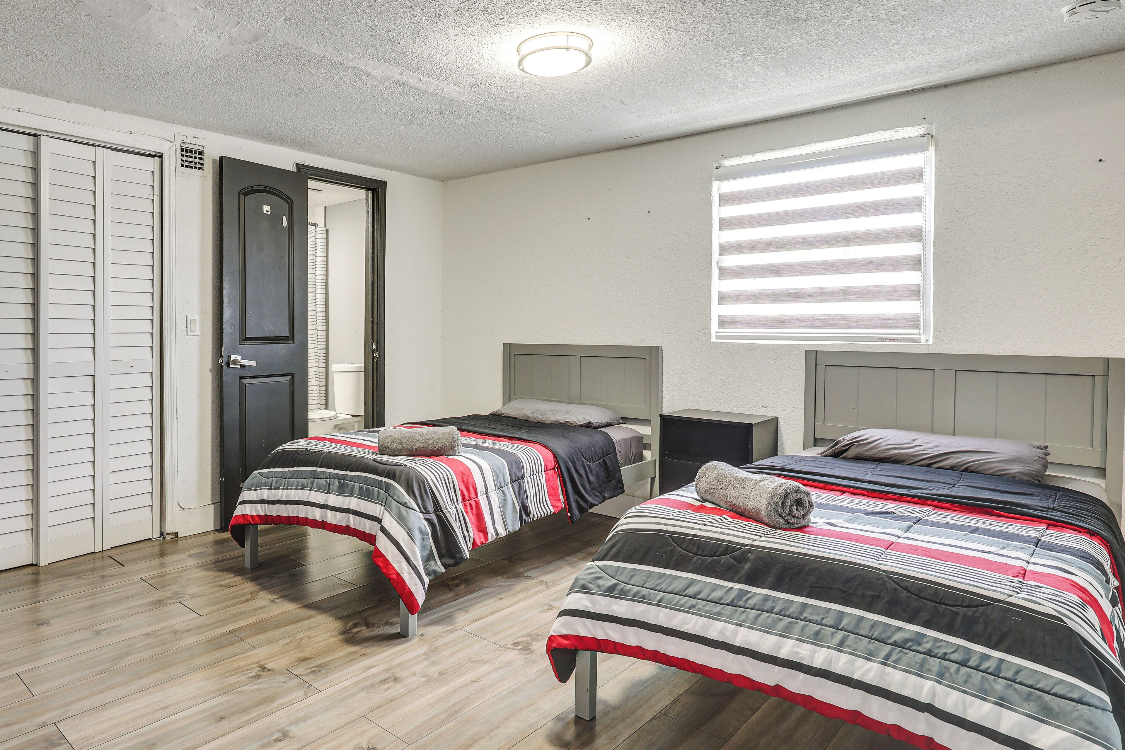 A room with two beds, a door, and a window with blinds.