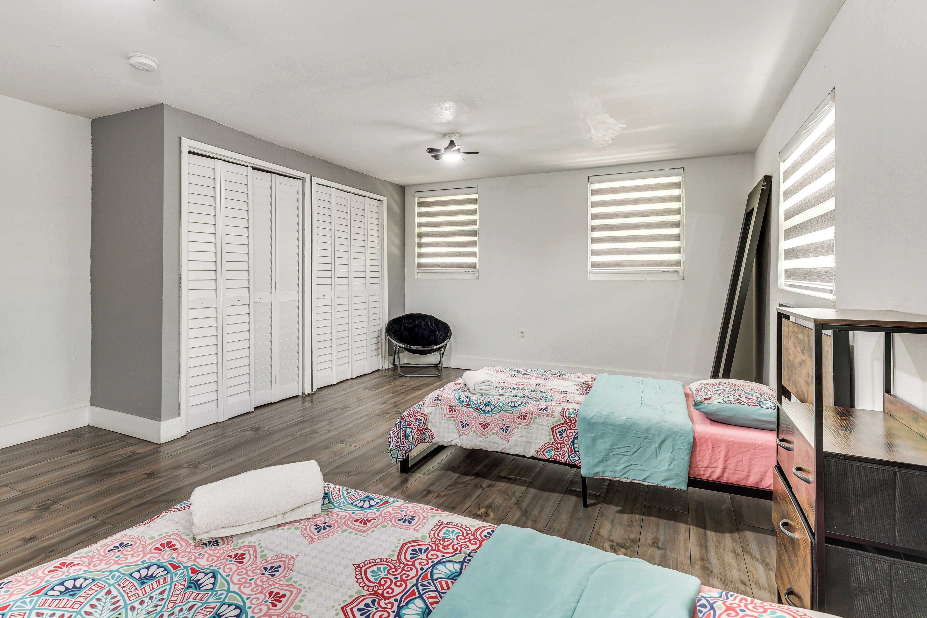 A bedroom with two beds, a wardrobe, a ceiling fan, and a window with blinds.