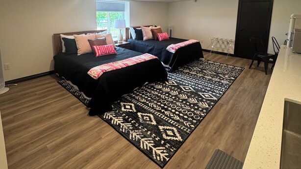 A bedroom with two beds, a window, a door, and a kitchenette. - Perfect place to stay for events at the Lazy E! (Guthrie)