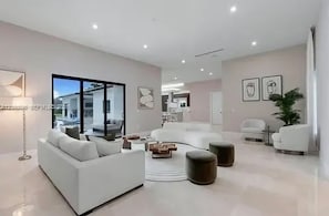 Un salon moderne avec un canapé blanc, une table basse et un coin repas à l’arrière-plan.