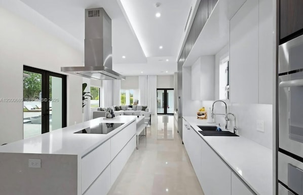 Une cuisine moderne avec des meubles blancs, un îlot central et une vue sur l’extérieur.