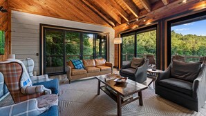 A wooden ceiling, large windows, a sofa, a table, and chairs in a room. - Swimming Bear Lodge - Lakefront | Platform Dock | Pet Friendly | Game Room (Cherry Log)