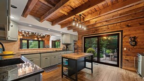 A modern kitchen with wooden beams, a central island, and a sliding glass door leading to an outdoor area. - Swimming Bear Lodge - Lakefront | Platform Dock | Pet Friendly | Game Room (Cherry Log)
