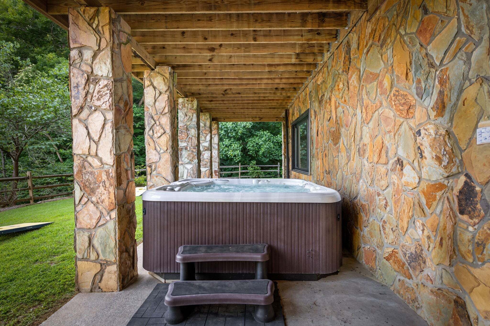 Un bain à remous situé dans un espace extérieur abrité, avec des murs en pierre et des poutres en bois.