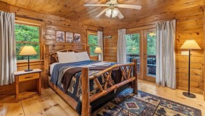 Une chambre dans une cabane en bois, avec un lit, deux lampes de chevet, un ventilateur de plafond et une vue sur l’extérieur.