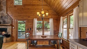 L’intérieur d’un chalet en bois est agrémenté d’une cheminée en pierre, d’une table à manger en bois et de grandes fenêtres.