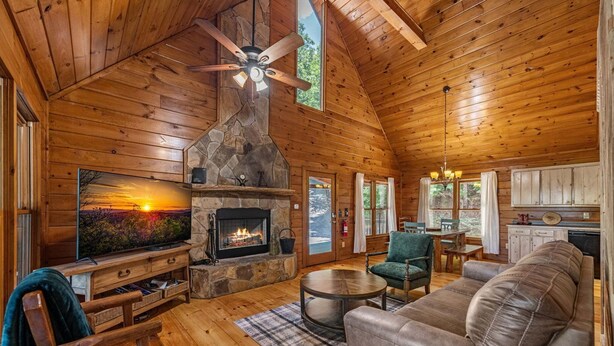 L’intérieur d’une cabane en rondins, avec une cheminée en pierre, des murs en bois, un ventilateur de plafond, un téléviseur, un canapé et un coin repas.
