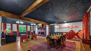 Een ruime kamer met een open haard, een eethoek met een tafel gedekt voor vier personen, en een groot raam met gordijnen.